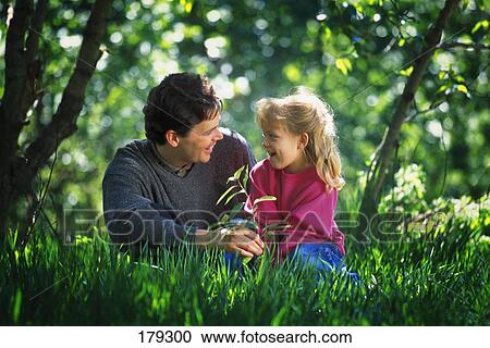 Stock Image - Father and daughter sitting in tall grass in park. Fotosearch