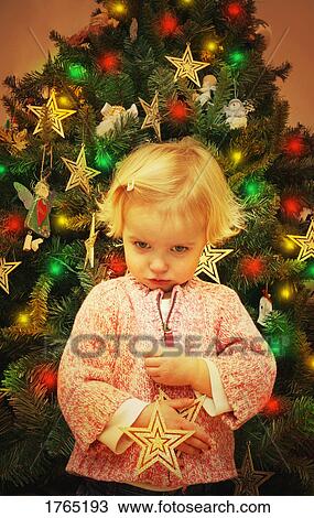 Stock Image - Child pouts in front of Christmas tree. Fotosearch