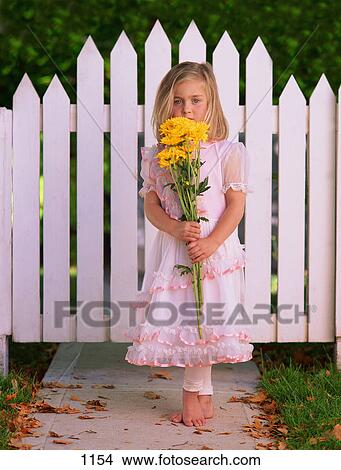 Picture - Girl with yellow flowers in front of picket fence. Fotosearch