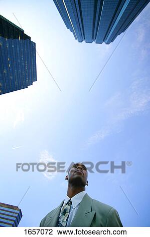 Stock Image - Businessman stands beside office tower. Fotosearch