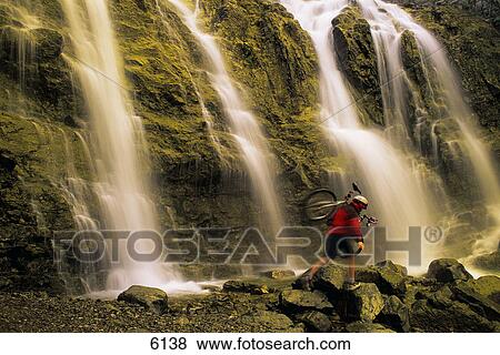 Stock Photo - Time delay of waterfall with cyclist carrying bicycle. Fotosearch
