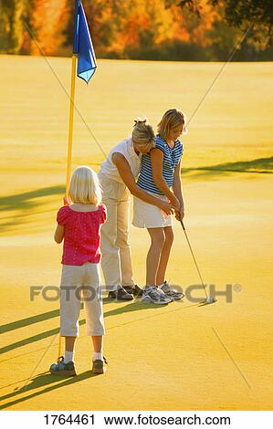 Stock Image - Mother shows daughter how to putt. Fotosearch