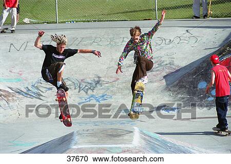 Boarders performing stunt at skate park View Large Photo Image Stock Image - Boarders performing stunt at skate park. Fotosearch