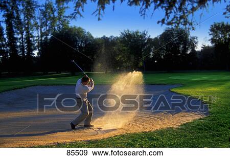 Stock Photo - Golfer chipping out of sand trap. Fotosearch