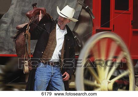 Stock Photo - Cowboy with saddle in front of stage coach. Fotosearch