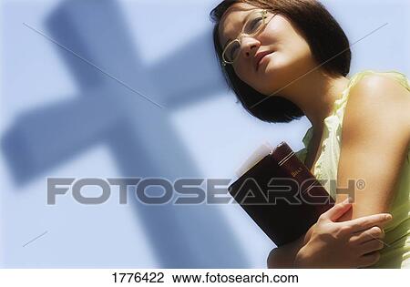 Stock Image - Woman holding bible with cross in background. Fotosearch