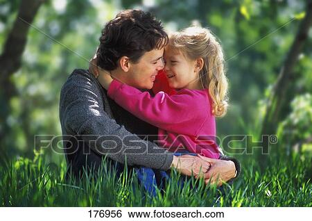 Stock Photograph - Father and daughter hugging in tall grass in park. Fotosearch