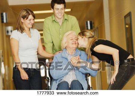 Stock Image - Young adults visiting a senior woman in a wheelchair. Fotosearch