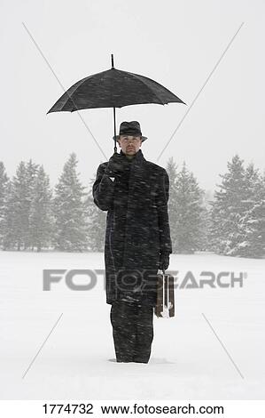Stock Image - Businessman waiting in the snow with umbrella and briefcase. Fotosearch