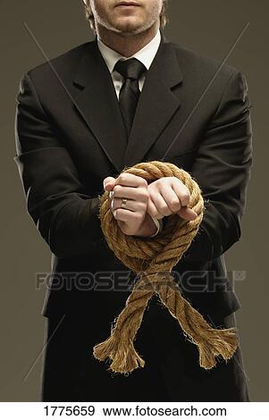 Stock Photo - Man in suit with hands tied with a large rope. Fotosearch