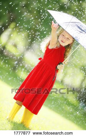 Stock Photo - A little girl walking in the rain under an umbrella, holding her hand out to feel the rain.. Fotosearch