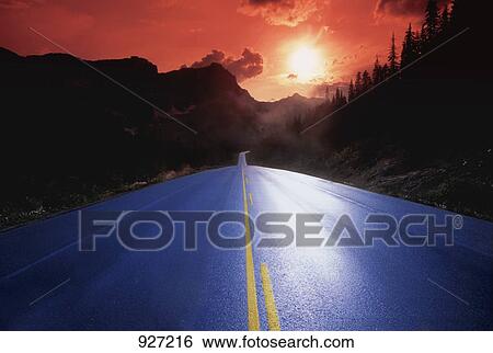 Stock Photograph - Road illuminated by sunrise/sunset. Fotosearch