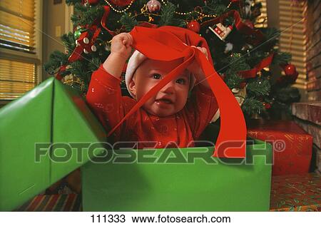 Stock Image - Toddler sitting in gift box playing with bow. Fotosearch