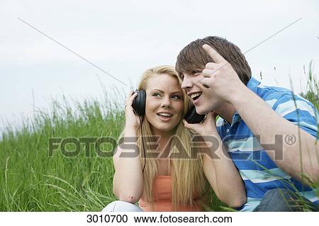 A young couple sitting in grass listening to music, low angle view View Large Photo Image Stock Image - A young couple sitting in grass listening to music, low angle view . Fotosearch