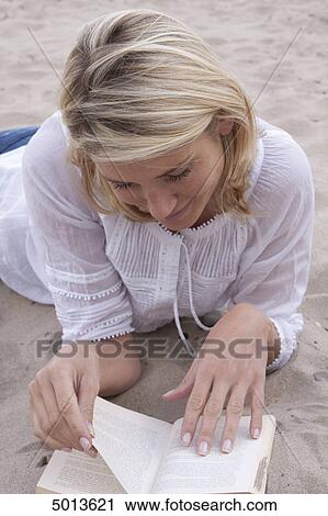 Stock Image - Blond woman reading book in sand . Fotosearch