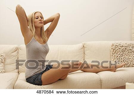 Picture - Blond young woman lifting her arms on couch . Fotosearch
