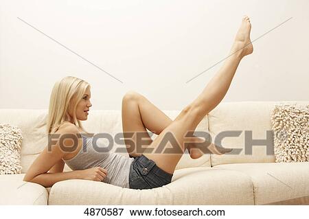 Blond young woman lifting her legs on couch View Large Photo Image Stock Photo - Blond young woman lifting her legs on couch . Fotosearch