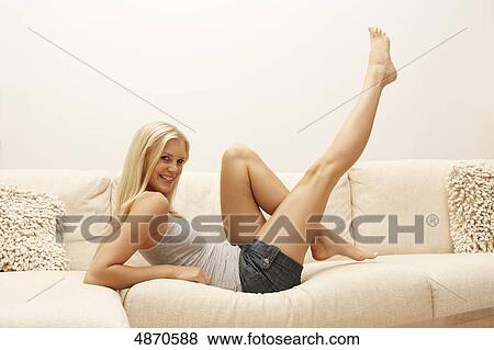 Stock Photo - Blond young woman lifting her legs on couch . Fotosearch