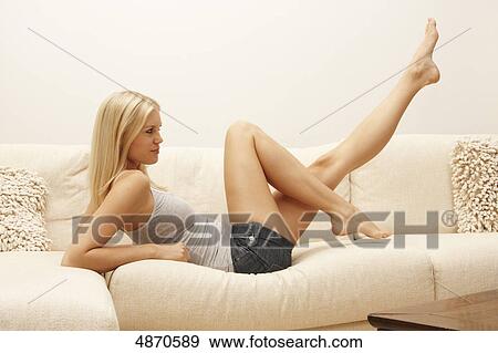 Stock Photo - Blond young woman lifting her legs on couch . Fotosearch