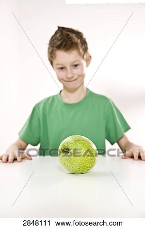 Stock Image - Boy looking at granny smith apple . Fotosearch
