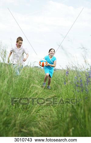 Stock Image - Brother and sister playing on a meadow, low angle view . Fotosearch