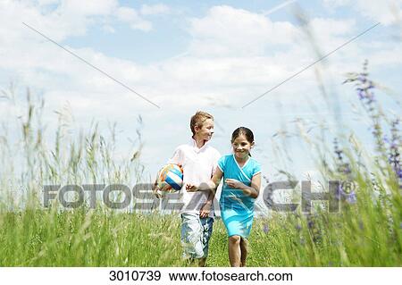 Stock Photo - Brother and sister playing on a meadow, low angle view, front view . Fotosearch