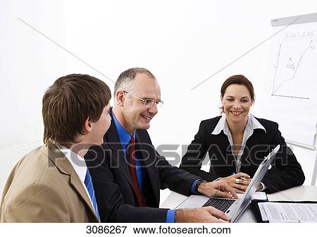 Stock Photo - Business people sitting at a table, looking at a laptop . Fotosearch