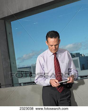 Businessman leaning against wall and using calculator View Large Photo Image Stock Photo - Businessman leaning against wall and using calculator . Fotosearch