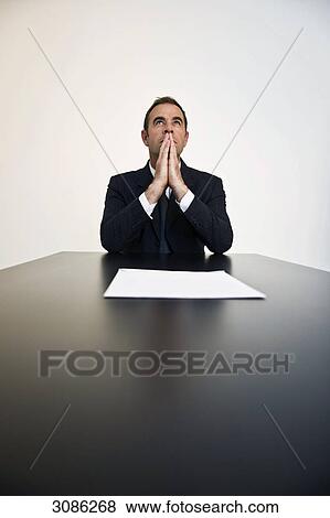 Businessman sitting at a table, hands covering mouth, front view View Large Photo Image Stock Photo - Businessman sitting at a table, hands covering mouth, front view . Fotosearch