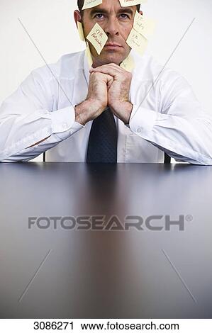 Stock Image - Businessman with post it notes at his face sitting at a table, front view, close-up . Fotosearch