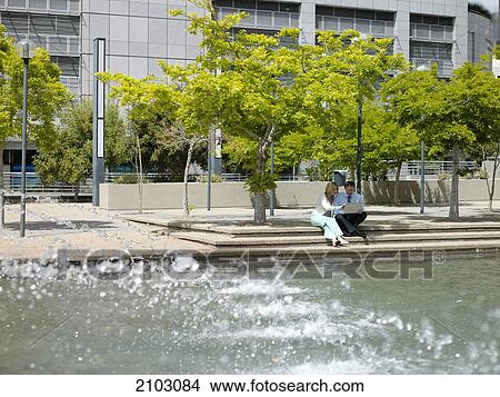 Businesswoman and businessman looking at laptop near fountain View Large Photo Image Picture - Businesswoman and businessman looking at laptop near fountain . Fotosearch