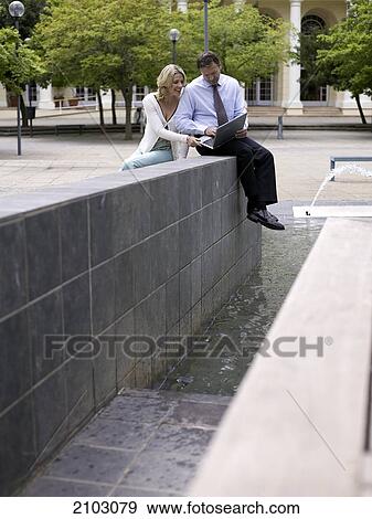 Businesswoman and businessman looking at laptop near fountain View Large Photo Image Stock Photo - Businesswoman and businessman looking at laptop near fountain . Fotosearch
