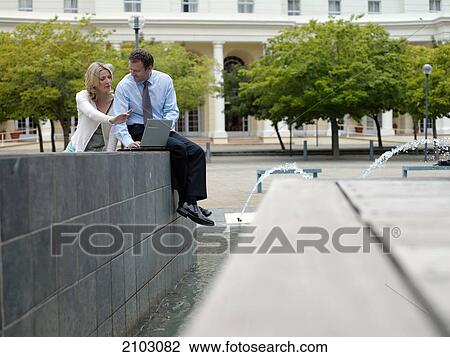 Businesswoman and businessman sitting near fountain with laptop View Large Photo Image Stock Image - Businesswoman and businessman sitting near fountain with laptop . Fotosearch
