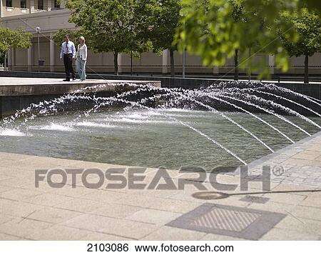 Businesswoman and businessman walking near fountain with laptop View Large Photo Image Stock Photograph - Businesswoman and businessman walking near fountain with laptop . Fotosearch