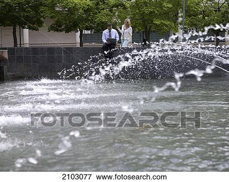 Businesswoman looking at businessman using laptop near fountain View Large Photo Image Stock Photo - Businesswoman looking at businessman using laptop near fountain . Fotosearch