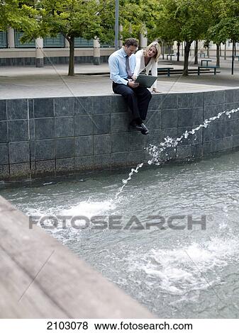 Businesswoman looking at businessman using laptop near fountain View Large Photo Image Stock Photo - Businesswoman looking at businessman using laptop near fountain . Fotosearch