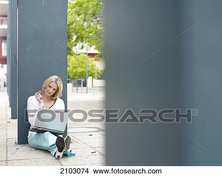 Picture - Businesswoman sitting at roadside and using laptop . Fotosearch