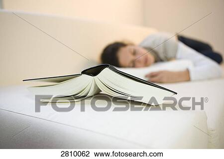 Stock Image - Close-up of book with girl lying on couch . Fotosearch