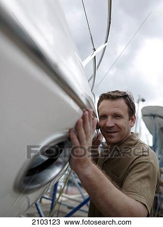 Stock Image - Close-up of man pushing boat at harbor . Fotosearch