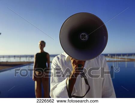Stock Image - Close-up of man using megaphone with woman standing in background . Fotosearch