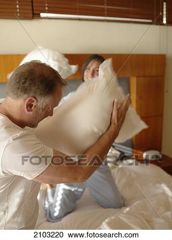 Stock Image - Couple having pillow fight on bed . Fotosearch