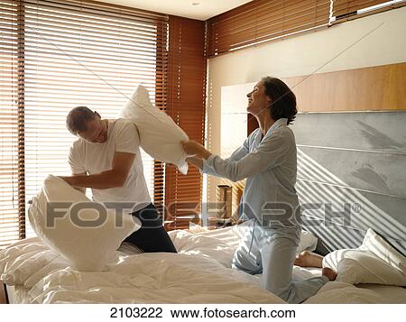 Stock Image - Couple having pillow fight on bed . Fotosearch