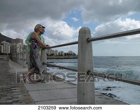 Stock Photo - Couple leaning on railing at coast . Fotosearch
