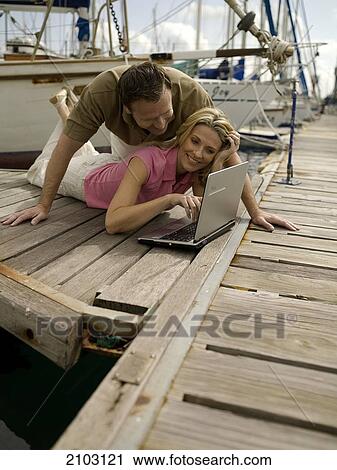 Couple looking at laptop on pier View Large Photo Image Stock Image - Couple looking at laptop on pier . Fotosearch