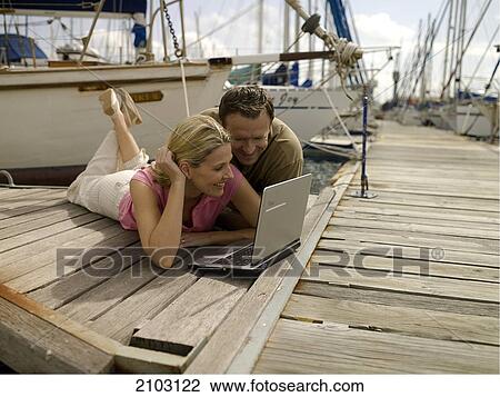 Couple looking at laptop on pier View Large Photo Image Stock Image - Couple looking at laptop on pier . Fotosearch