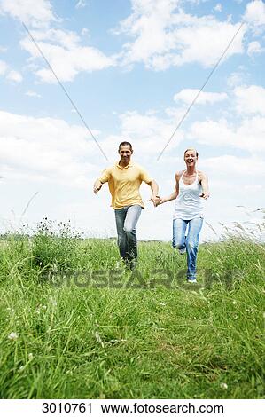 Stock Image - Couple running over a meadow, low angle view, front view . Fotosearch