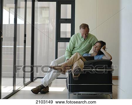 Couple sitting on armchair and looking at laptop View Large Photo Image Stock Photo - Couple sitting on armchair and looking at laptop . Fotosearch