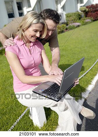 Stock Image - Couple using laptop at front yard . Fotosearch