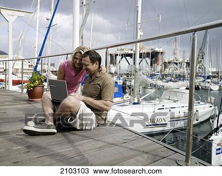 Stock Image - Couple using laptop at harbor . Fotosearch