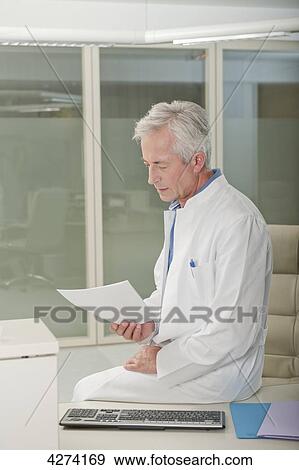 Stock Photo - Doctor at desk reading document . Fotosearch